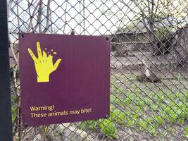 Warning sign on zoo enclosure fence showing bitten hand and message. These animals may bite to caution visitors and promote safety awareness around wild animals photo