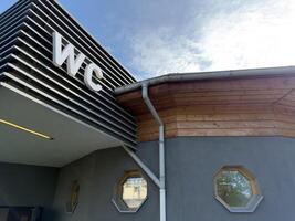 Exterior view of public restroom with large WC sign, modern horizontal paneling, wooden roof trim and octagonal windows, representing clean architectural solution for functional city service building photo