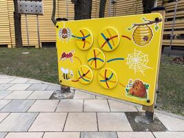 Outdoor educational panel on playground with yellow insect themed activity board showing spider, ant, bee, hive, web, and ant hill, designed for children learning, fun, and motor skill development photo