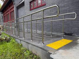 Stainless steel accessibility ramp with bright yellow tactile paving for visually impaired individuals, located next to building, highlighting inclusive design and care for people with disabilities photo