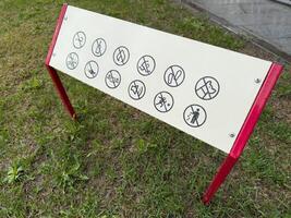 Information board with multiple prohibition icons installed on grass. The sign uses universal symbols to indicate restricted actions in a public area, promoting safety and proper behavior photo