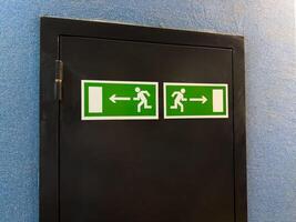 Minimalist composition with two symmetrical emergency exit signs on black panel against blue wall, combining graphic clarity and functional interior detail in modern public space or institution photo