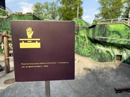 Warning sign in a zoo asking visitors not to place children on the barrier for safety. Clear multilingual notice helps prevent accidents in animal enclosures and ensures safe behavior photo