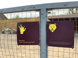 Warning signs on enclosure with dangerous animal in zoo. Inscription on sign about warning about biting animal. Concept of safety rules of visiting zoo. Do not feed the animals in cage, they can bite photo