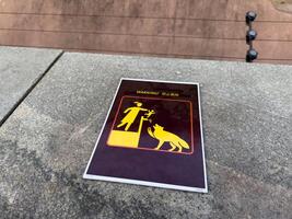 Caution sign with bright yellow pictogram warning about danger of lifting children near wild animals, placed on stone surface in zoo area, serving as visual safety reminder for visitors and families photo