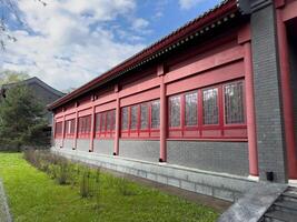 Side view of traditional Chinese style building with red columns and patterned windows, showcasing cultural architecture with clean lines and symmetrical structure in urban environment photo