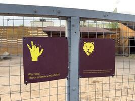 Sign on cage in zoo with warning symbol about biting animal in the enclosure. Notifying visitors about the danger of wild animals. Safety when visiting zoo. The animal may bite photo