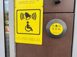 Inclusive access button with Braille and symbols for wheelchair users, elderly people and parents with strollers, mounted near entrance and designed for equal usability in modern public spaces photo