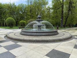 Classic tiered stone fountain with circular design and symmetrical water streams in public park. Decorative water feature as focal point of landscaped pedestrian zone photo