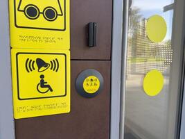 Accessibility call system with yellow tactile and audio symbols, including Braille text and assistance button near glass door, designed to support people with disabilities in modern infrastructure photo