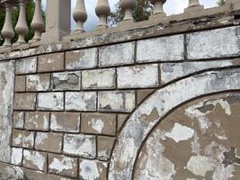 Old textured brick wall with crumbling plaster and flaking paint shows deep signs of wear and weathering, creating a visually rich architectural background suitable for texture or design use photo