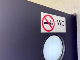 Closeup of WC door with round frosted window and no smoking sign on white label, showing clear visual message for public restroom users in clean and modern architectural setting photo