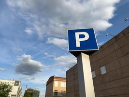 Large, bold blue P parking sign stands tall in the foreground of an industrial style urban building, framed by dramatic sky and scattered clouds, highlighting the practical side of city architecture photo