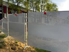 Temporary metal fencing with red warning lights ensures public safety during outdoor construction work. The perforated panels and stable supports indicate organized protective measures photo