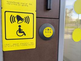 Yellow tactile signage and assistance button with bell and disability symbols including Braille, providing accessible user interface near modern entrance for inclusive and barrier free access photo