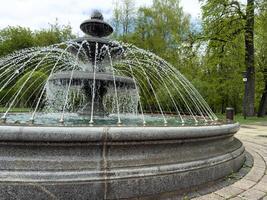 Close up of stone fountain with layered tiers and arched water jets in public park. Clear focus on textured surface and dynamic water flow design photo