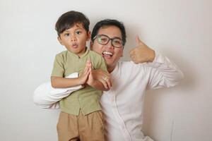 Joyful and happy Asian dad playing with his little son in the living room, piggyback, spending fun time together at home. photo