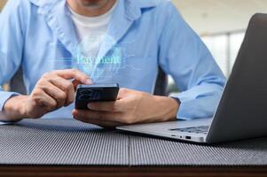 Man Using Smartphone for Digital Payment with Laptop in Background photo