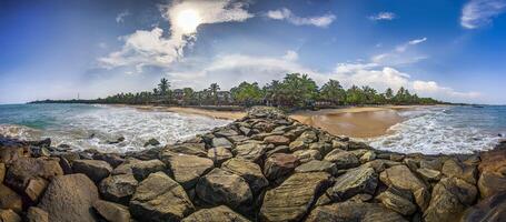 Rocky jetty at sunny Tangalle beach with palm trees and ocean waves photo