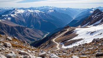 a high mountain pass with snow capped peaks all around, and a narrow trail winding through the rocky terrain. photo