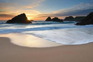 A beach with waves and rocks at sunset photo