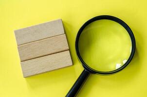 Magnifying glass against a bright yellow background with customizable space on wooden block for text photo