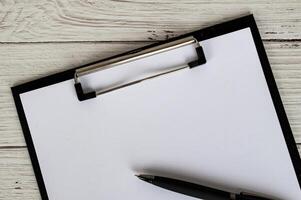 Top view of a blank clipboard with a sheet of white paper and a black pen. Copy space concept photo