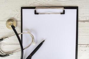 Top view of a blank clipboard with a sheet of white paper and doctor stethoscope. Copy space concept. photo