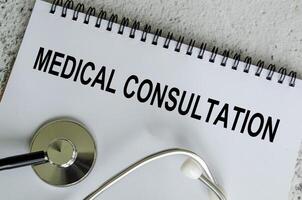Top view of Medical Consultation Text on white paper notepad with stethoscope on wooden table background. Health and medical concept. photo