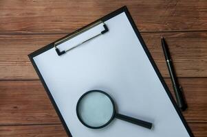 Top view of white paper clipboard with magnifying glass and a black pen. Copy space concept. photo