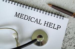 Top view of Medical Help text on white paper notepad with stethoscope on wooden table background. Health and medical concept. photo