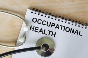 Top view of Occupational Health text on white paper notepad with stethoscope on wooden table background. Health and medical concept. photo