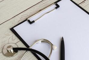 Side view of blank clipboard with a sheet of white paper and doctor stethoscope. Copy space concept. photo