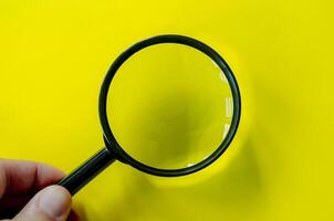 Top view of a magnifying glass against a bright yellow background. Searching, examining, focusing or investigation concept. photo