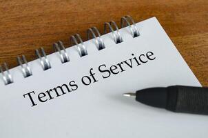 Terms of Service text on white notepad with wooden table background. Terms of Service concept. photo