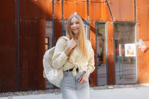 Young woman smiles while standing in front of modern architecture during the day with a backpack photo