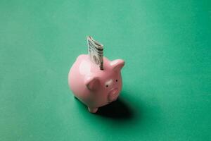 Piggy bank shown with cash inserted on green background displays the importance of saving money for financial security and goals photo