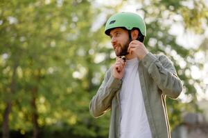Man putting on a green helmet while preparing for a biking adventure in a sunny park during the afternoon photo