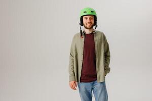 Young man in a green helmet stands confidently in a studio setting with a neutral backdrop, showcasing safety and style in casual attire photo