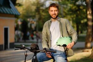 Smiling man in green helmet prepares for cycling in a sunny park setting during the afternoon photo