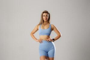 Fitness enthusiast poses confidently in light blue activewear in a minimalistic studio setting during daytime photo
