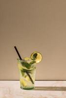 Close-up of a glass of delicious mojito with lime and fresh mint. Tasty lemonade with ice cubes on a marble table. A cup of cool citrus cocktail and a straw. photo