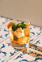 Close-up of a glass of mineral water with peach and fresh mint on the table with patterned tiles. A cup of cool, delicious, healthy drink with ice cubes. photo