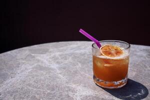 Close-up of a delicious citrus cocktail in a glass on a marble round table. A cup of carbonated drink with a straw and a slice of orange. photo