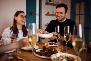 A young woman and a man are drinking champagne and eating in the living room. A happy couple family dinner. A husband and wife are having lunch and laughing at a set table. photo