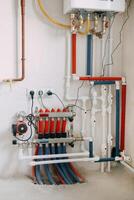 Detailed view of an intricate heating system setup featuring red and blue color-coded pipes, valves, and gauges. Connection diagram of a gas boiler with a underfloor heating system. photo