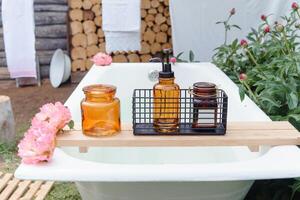 Outdoor bathtub with soap bottle, candle, and pink flowers for a luxurious self-care experience in nature. Relaxation and spa concept for escape and wellness. photo