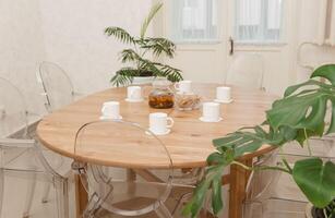 Cozy dining setting featuring round wooden table surrounded by transparent chairs, complemented by lush green potted plants, creating a warm and inviting interior atmosphere photo