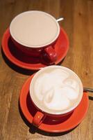 Cups of coffee in vibrant red ceramic mugs with intricate surface designs, resting on a smooth wooden table, evoking warmth and inviting sharing moment photo
