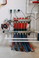 Central heating system image showing multiple red and blue pipes connected to control panel with valves and gauges. System is set up against plain wall. Underfloor heating system photo
